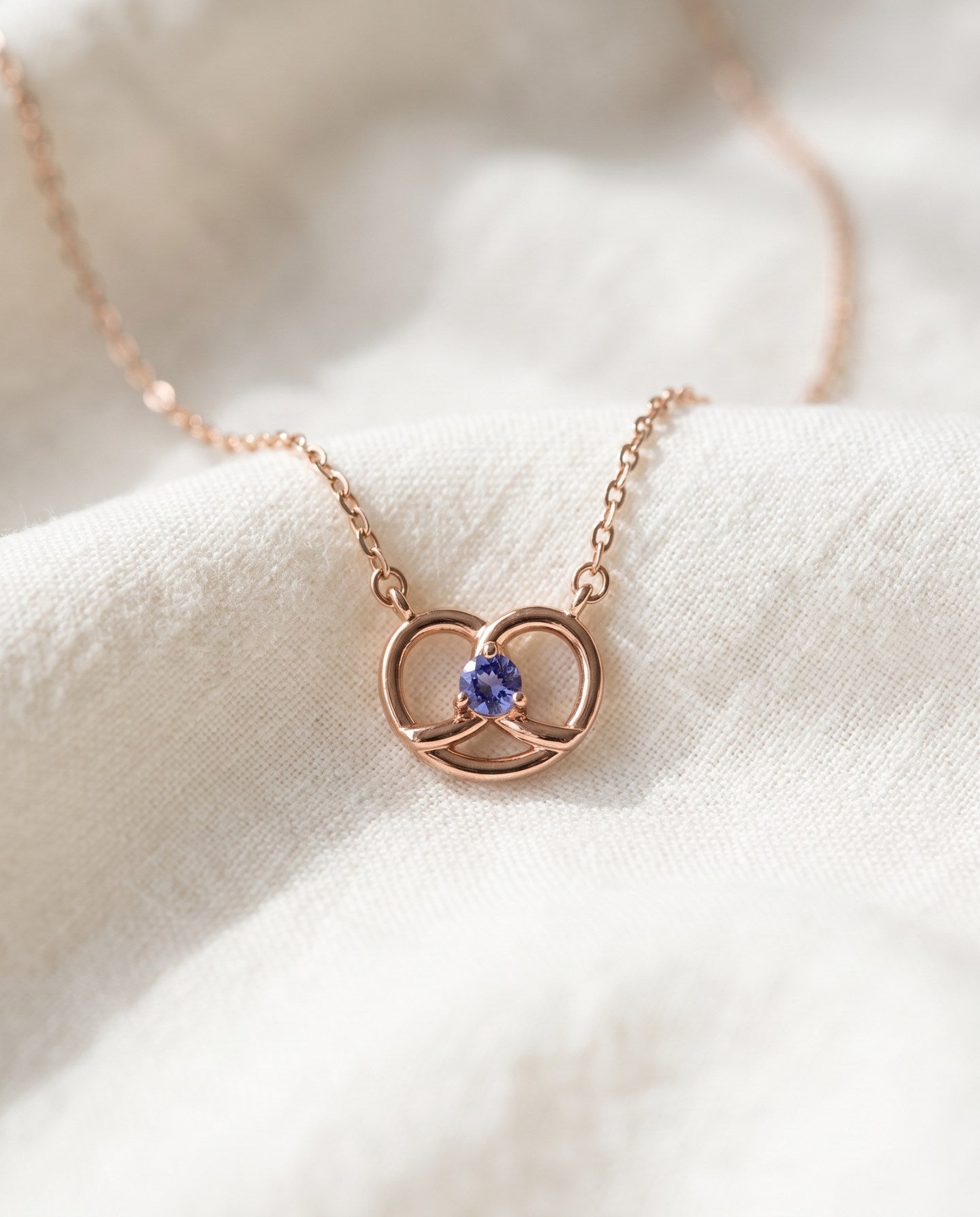Croissant Heart Tanzanite Necklace in rose gold, arranged with its cable chain on soft ivory fabric