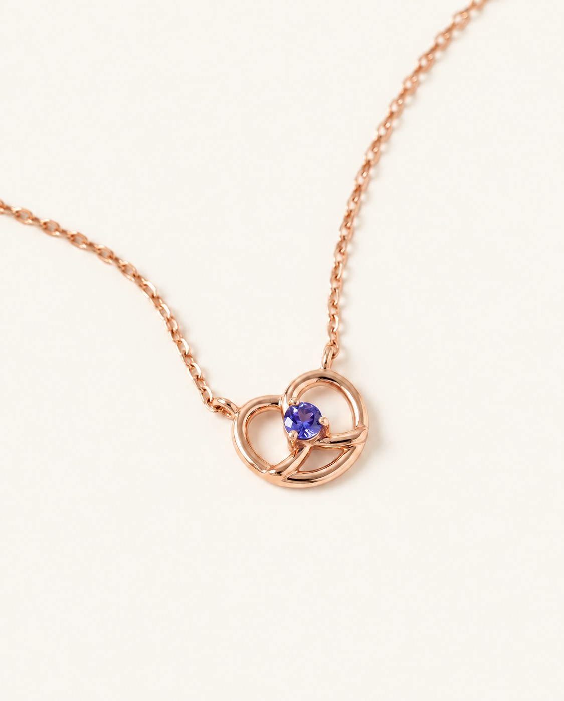 Croissant Heart Tanzanite Necklace in rose gold, front view of the open heart pendant on warm ivory
