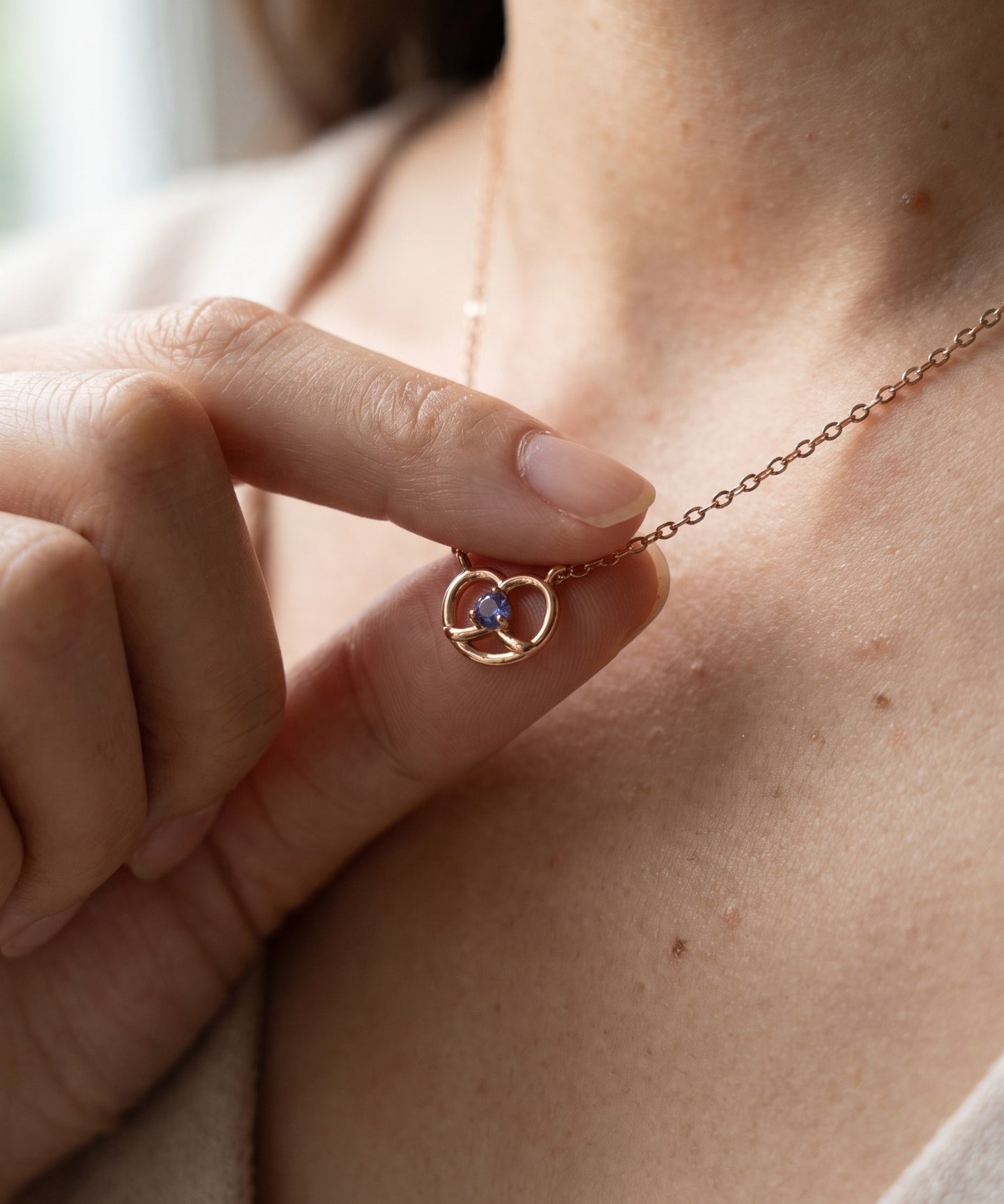 Croissant Heart Tanzanite Necklace in rose gold, held gently at the neckline in natural light