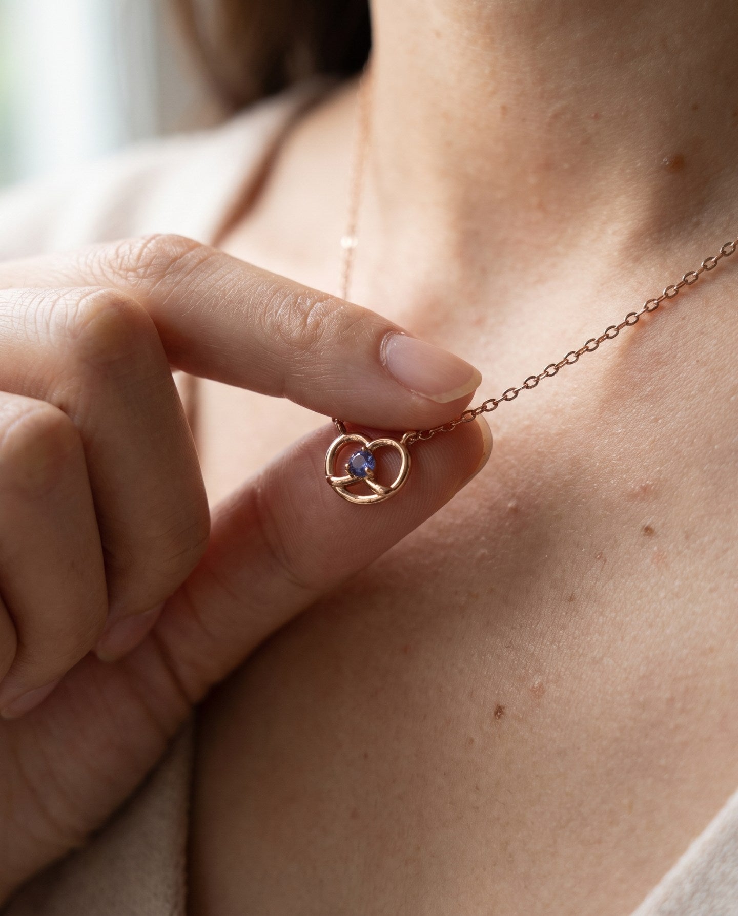Croissant Heart Tanzanite Necklace in rose gold, held gently at the neckline in natural light