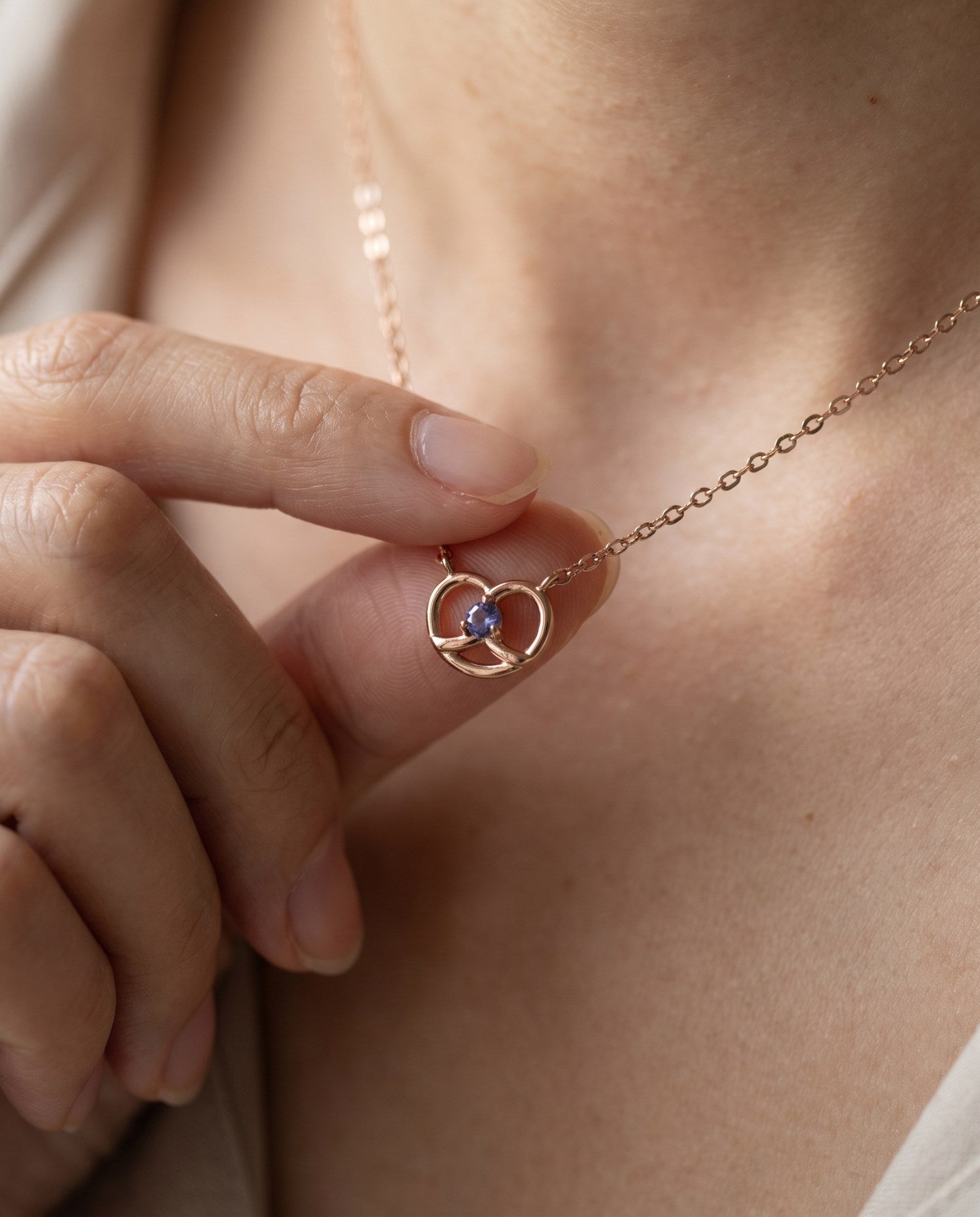 Croissant Heart Tanzanite Necklace in rose gold, worn at the neckline with the pendant held between fingers
