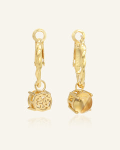 Close-up of the Golden Luck Hoops in yellow gold, resting on a warm linen background