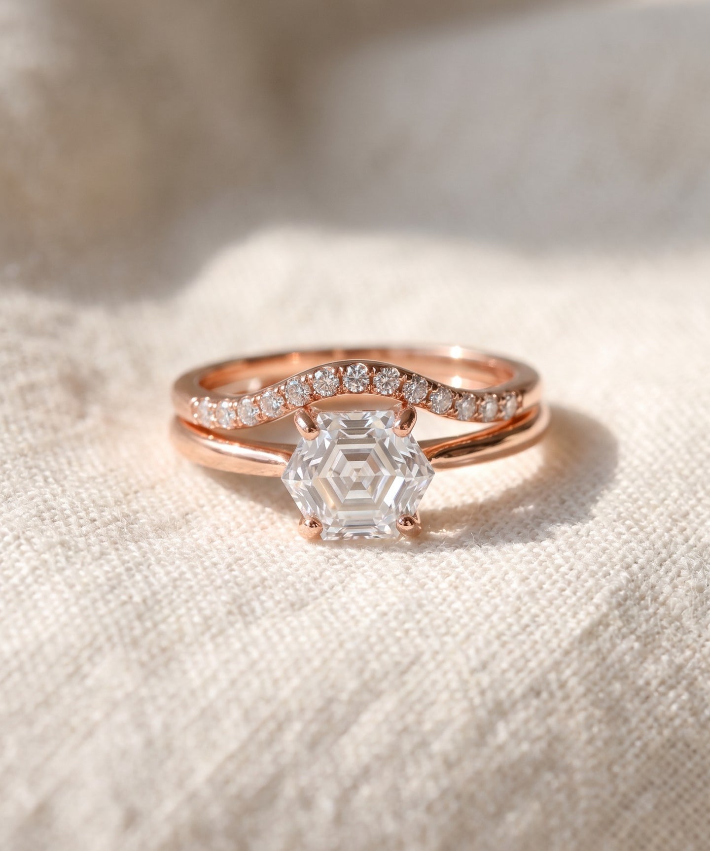 Hexagon step-cut moissanite ring in rose gold styled on ivory linen with stacking rings