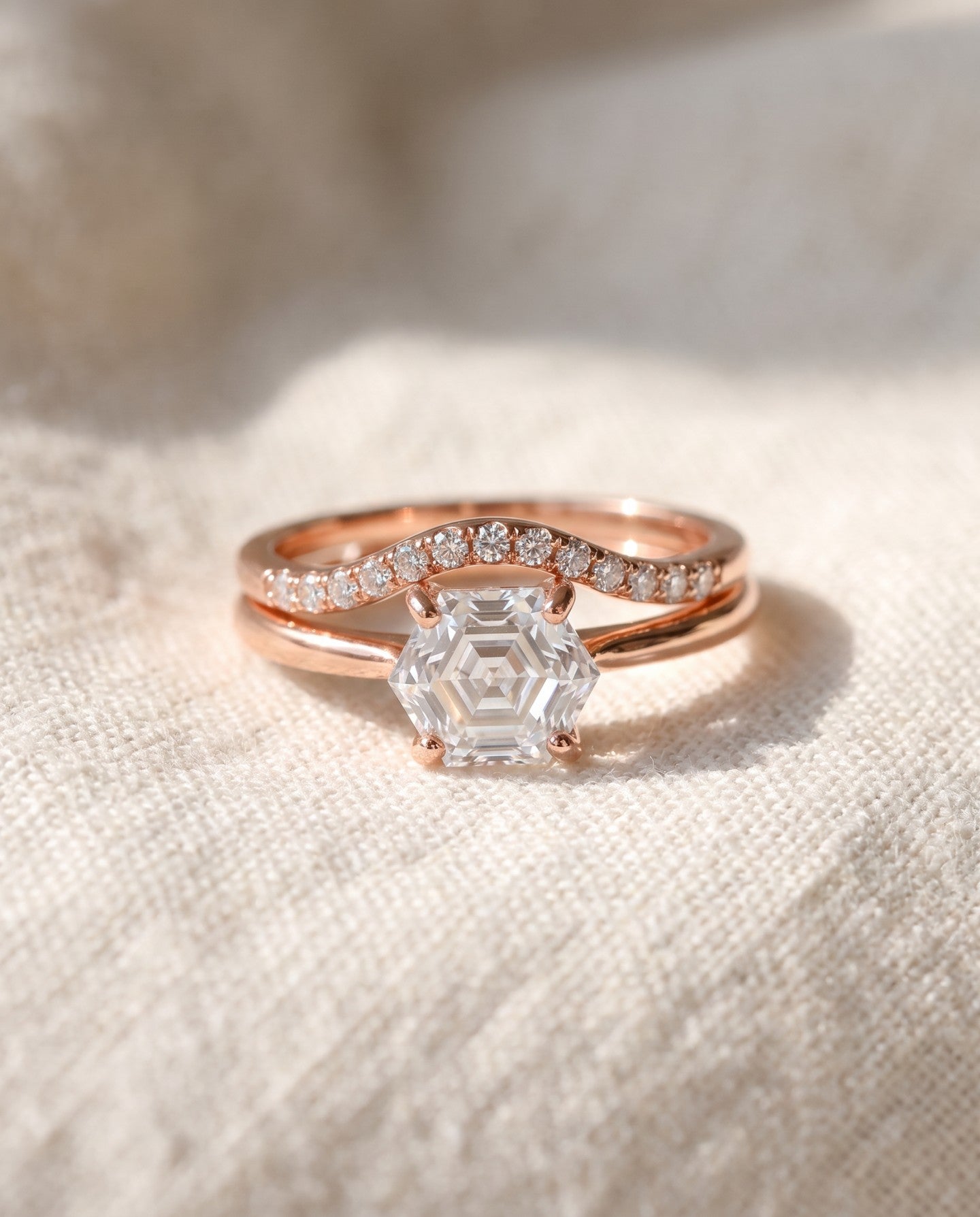 Hexagon step-cut moissanite ring in rose gold styled on ivory linen with stacking rings