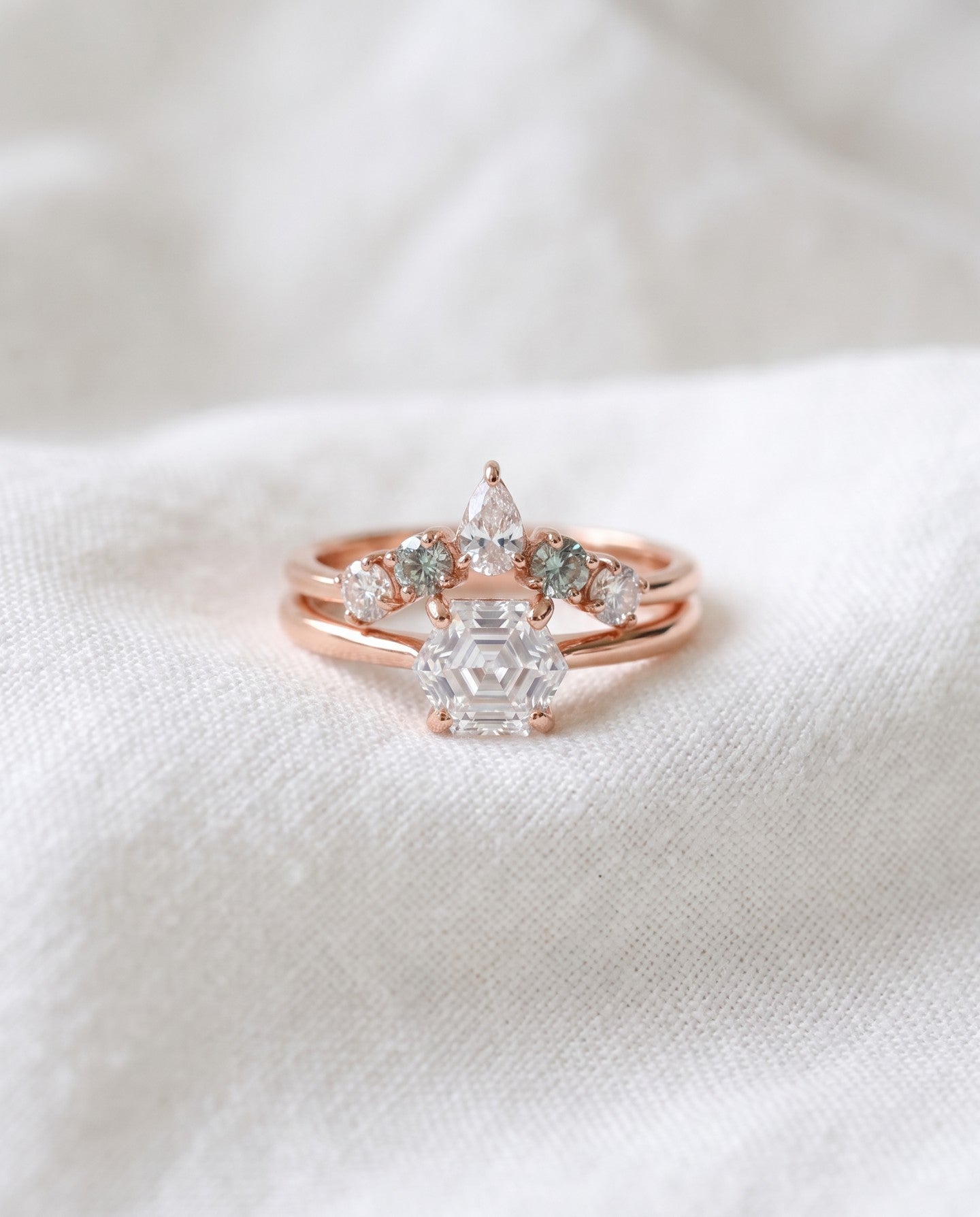 Hexagon step-cut moissanite ring in rose gold styled on ivory linen with stacking rings