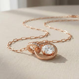 Close-up of rose gold interlocking rings moissanite necklace on a beige surface