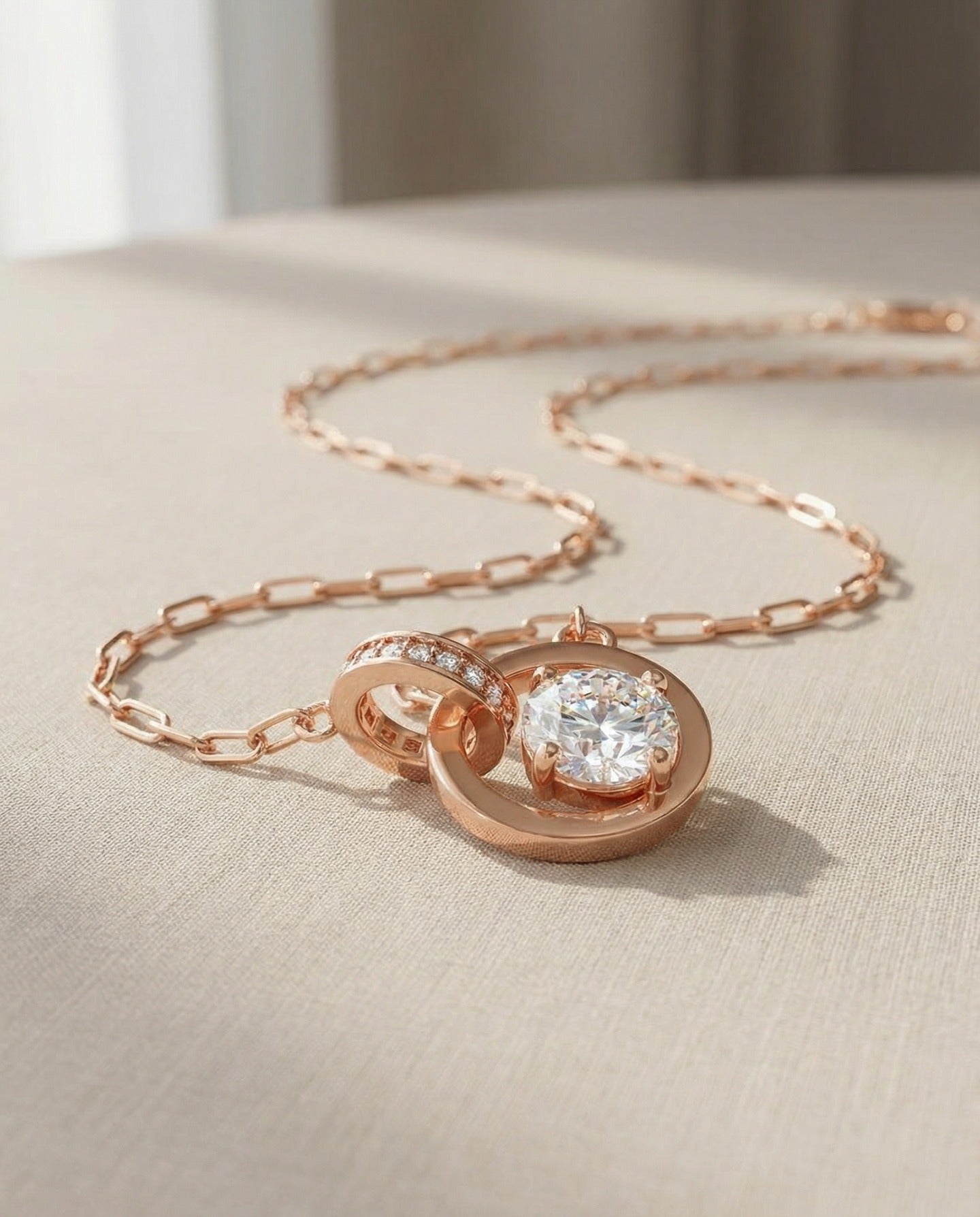 Close-up of rose gold interlocking rings moissanite necklace on a beige surface