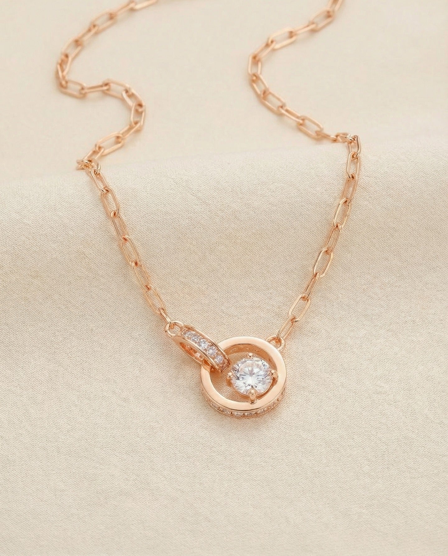 Rose gold interlocking rings moissanite necklace laid flat on ivory
