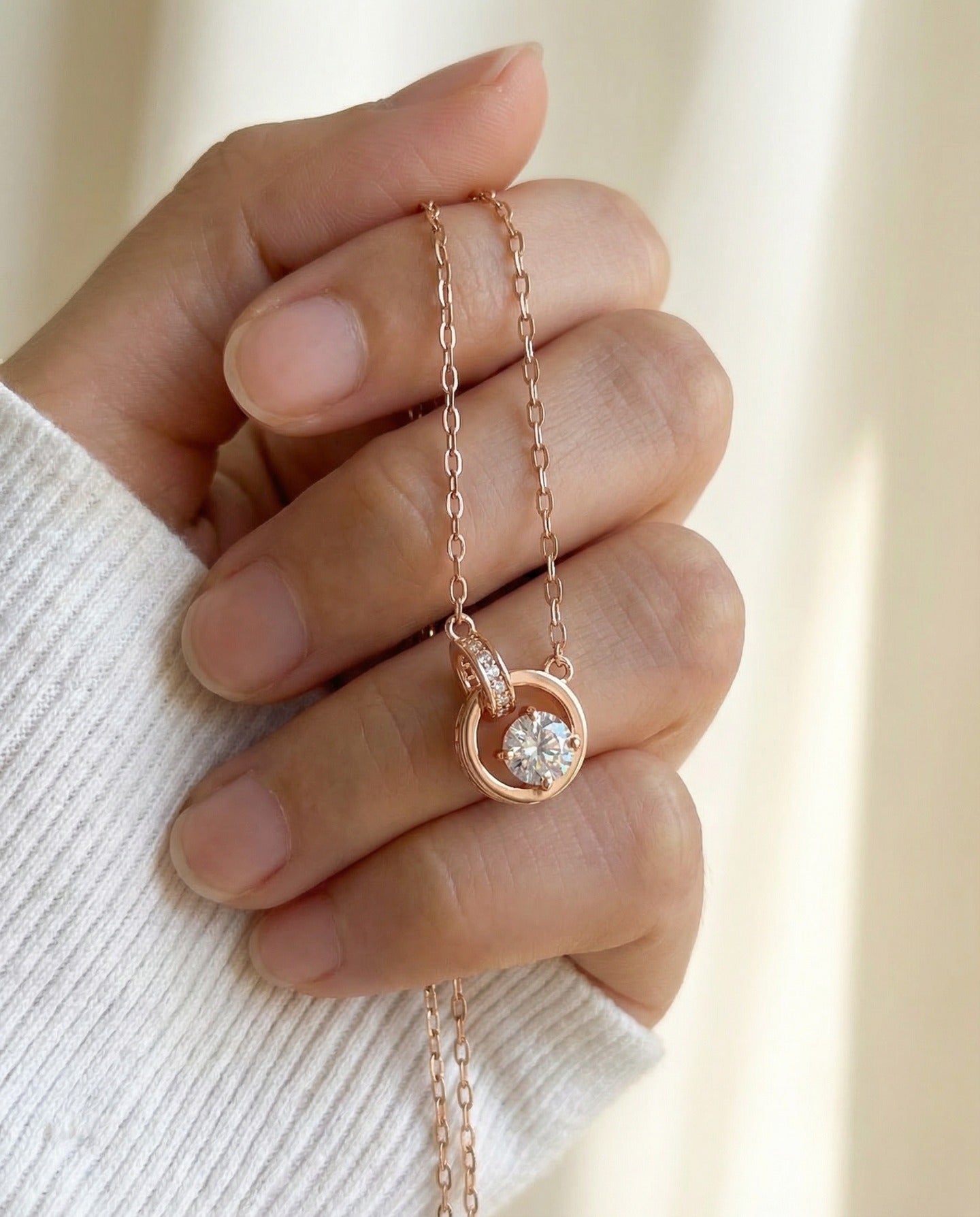 Rose gold interlocking rings moissanite necklace held in a hand