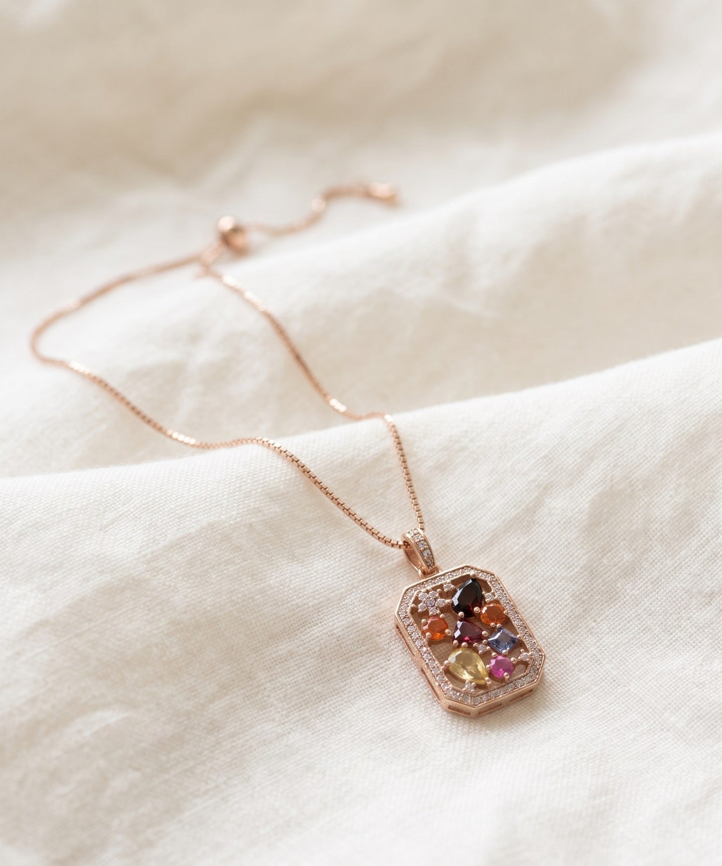 Jewel Box Multi-Gemstone Necklace in rose gold, arranged on ivory linen with its box chain