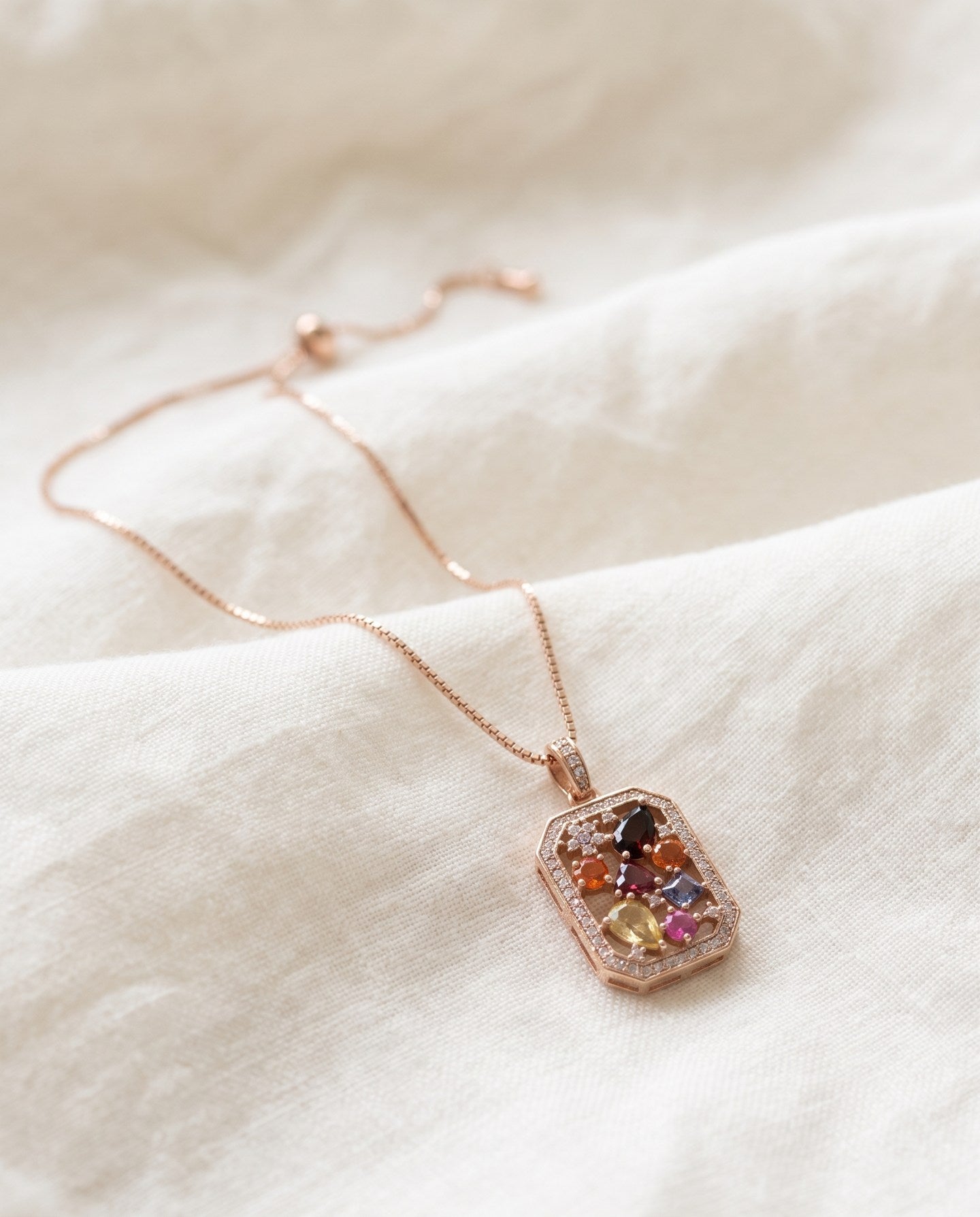 Jewel Box Multi-Gemstone Necklace in rose gold, arranged on ivory linen with its box chain