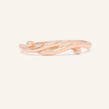 Knots End Ring in rose gold, front view of the intertwined knot band on warm ivory