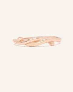 Knots End Ring in rose gold, front view of the intertwined knot band on warm ivory