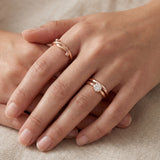 Knots End Ring in rose gold, worn on a hand beside a pearl ring