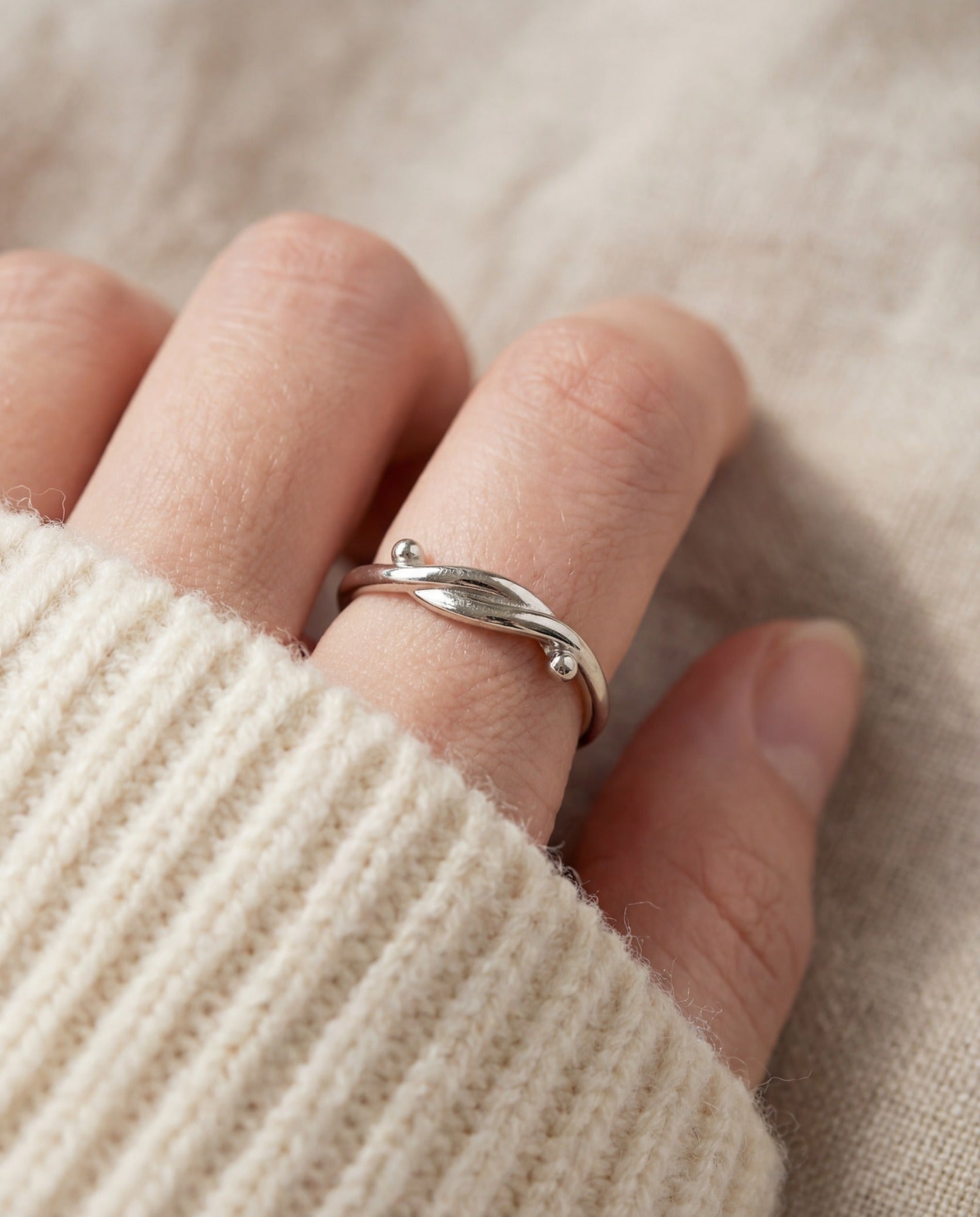 Knots End Ring in silver, close-up worn on a hand with an ivory knit sleeve