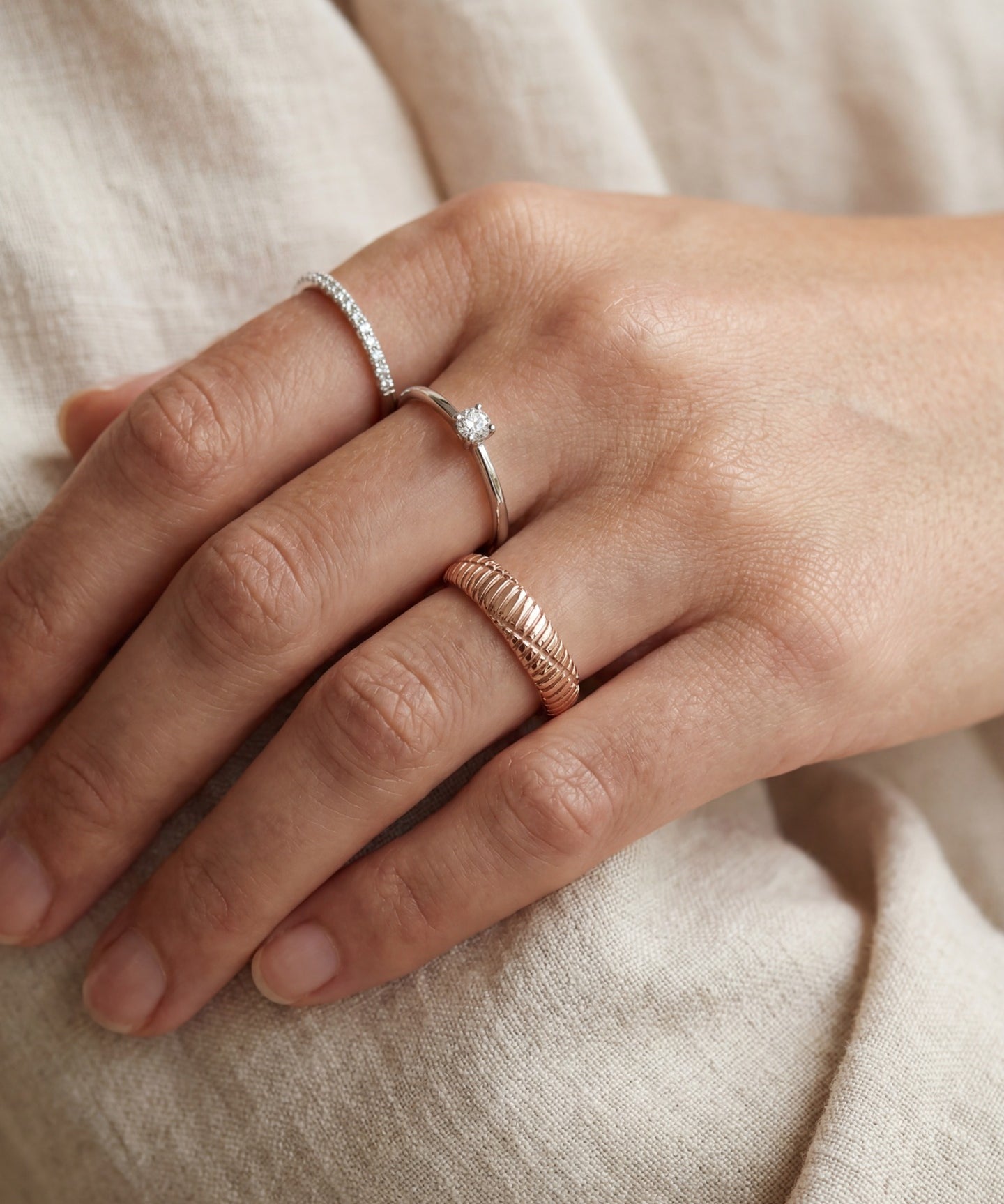 Linear Stripes Band in rose gold, worn on a hand beside two delicate rings against cream fabric