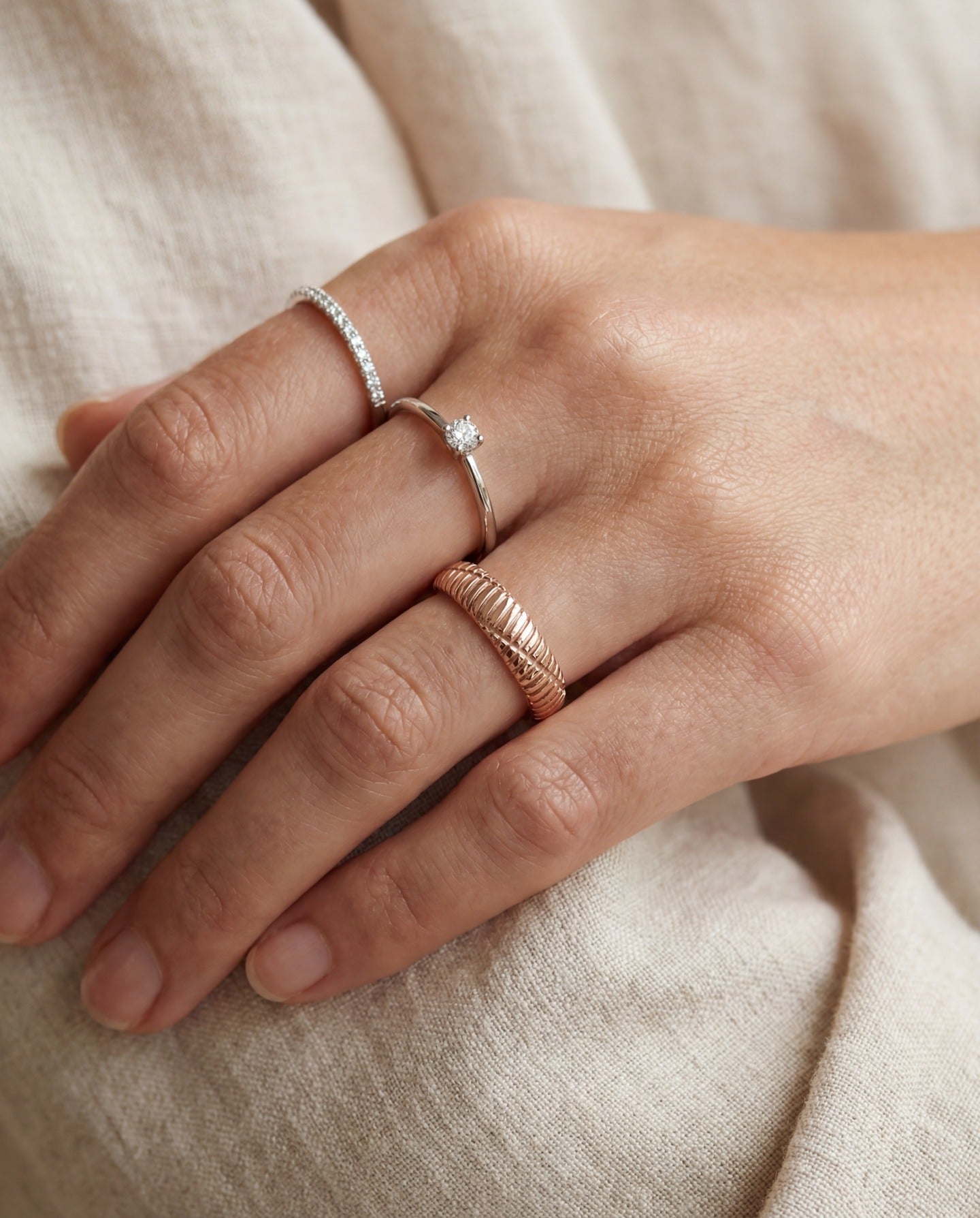 Linear Stripes Band in rose gold, worn on a hand beside two delicate rings against cream fabric