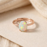 Luna Ethiopian Opal Ring in rose gold, oval opal ring resting on a cream surface beside a knit sleeve