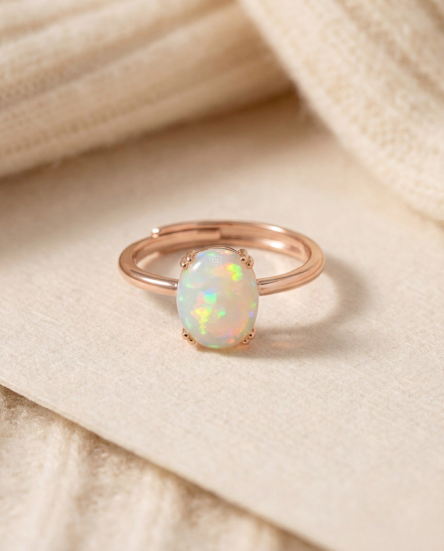 Luna Ethiopian Opal Ring in rose gold, oval opal ring resting on a cream surface beside a knit sleeve