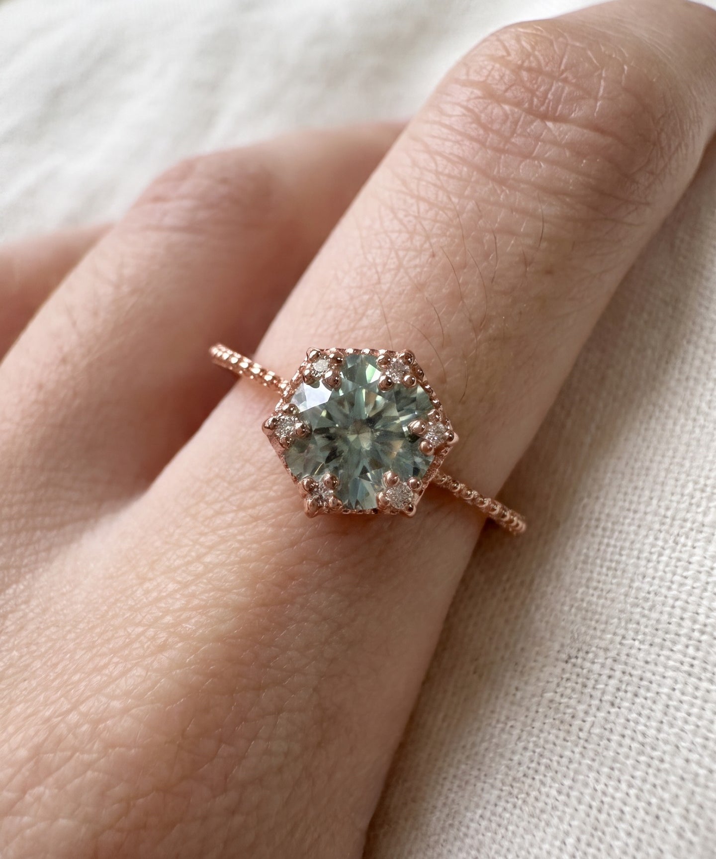 Rose gold mint green moissanite floral halo ring worn on a hand