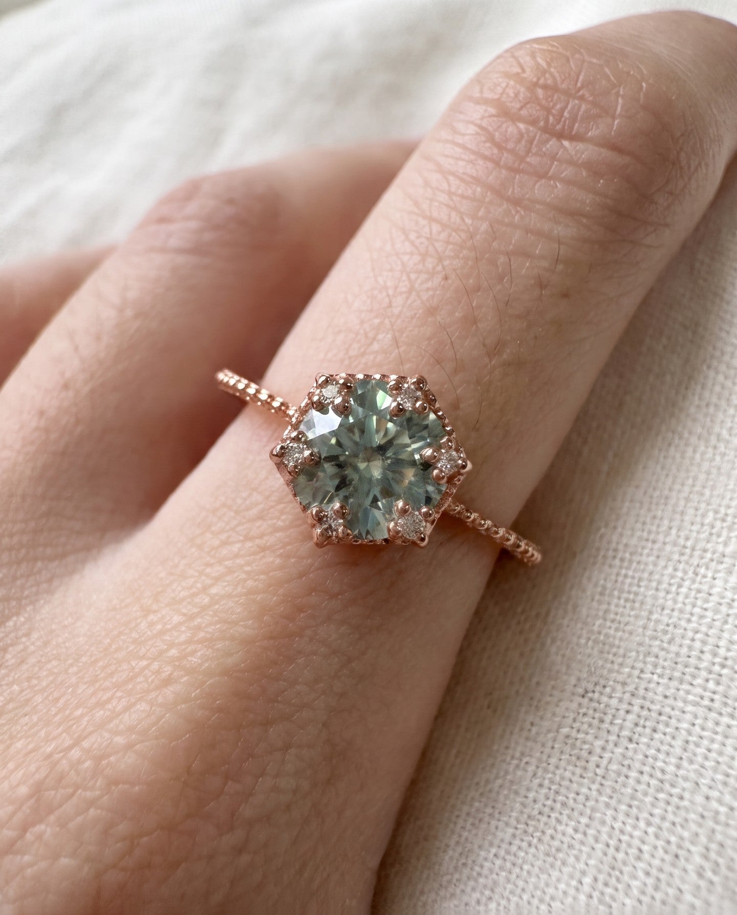 Rose gold mint green moissanite floral halo ring worn on a hand