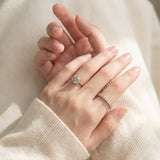 Mint green moissanite floral halo ring worn with delicate stacking rings and an ivory knit sleeve