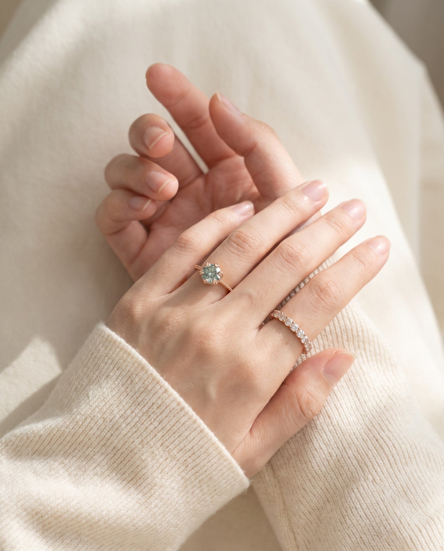 Mint green moissanite floral halo ring worn with delicate stacking rings and an ivory knit sleeve