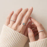 Mint green moissanite floral halo ring worn with delicate stacking rings and an ivory knit sleeve