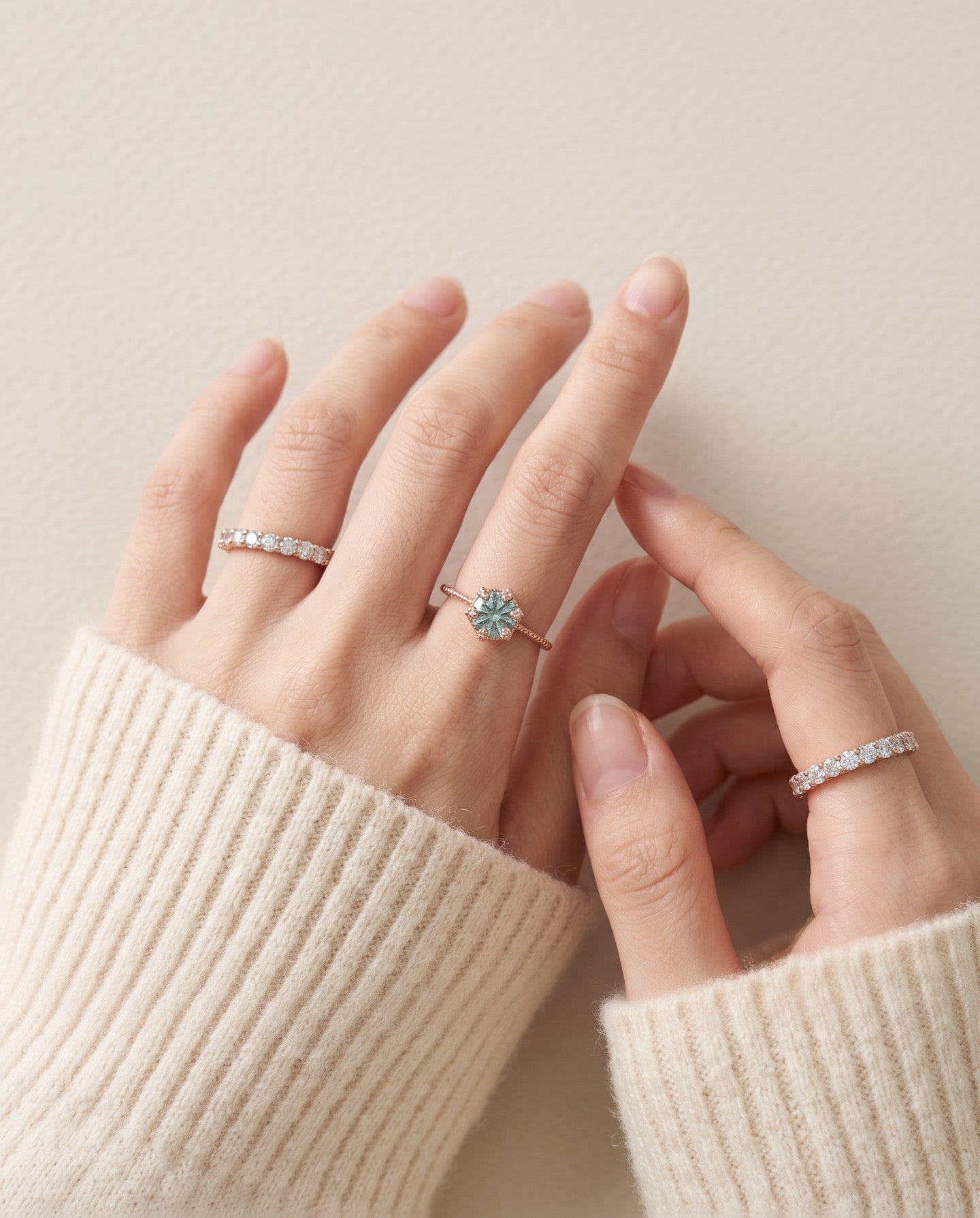 Mint green moissanite floral halo ring worn with delicate stacking rings and an ivory knit sleeve