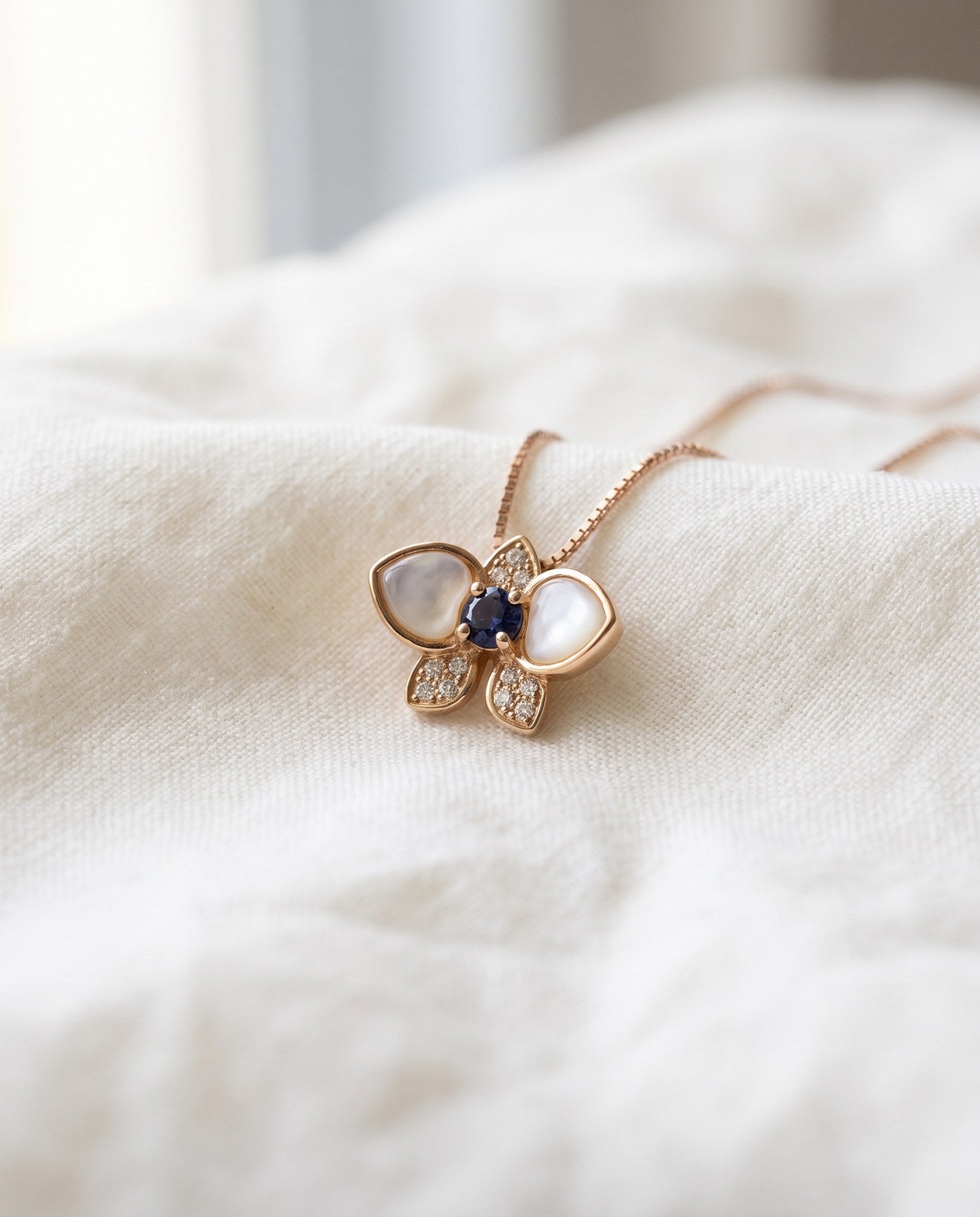 Orchid Bloom Mother of Pearl Necklace in rose gold with iridescent wings and purple spinel centre on a soft ivory background