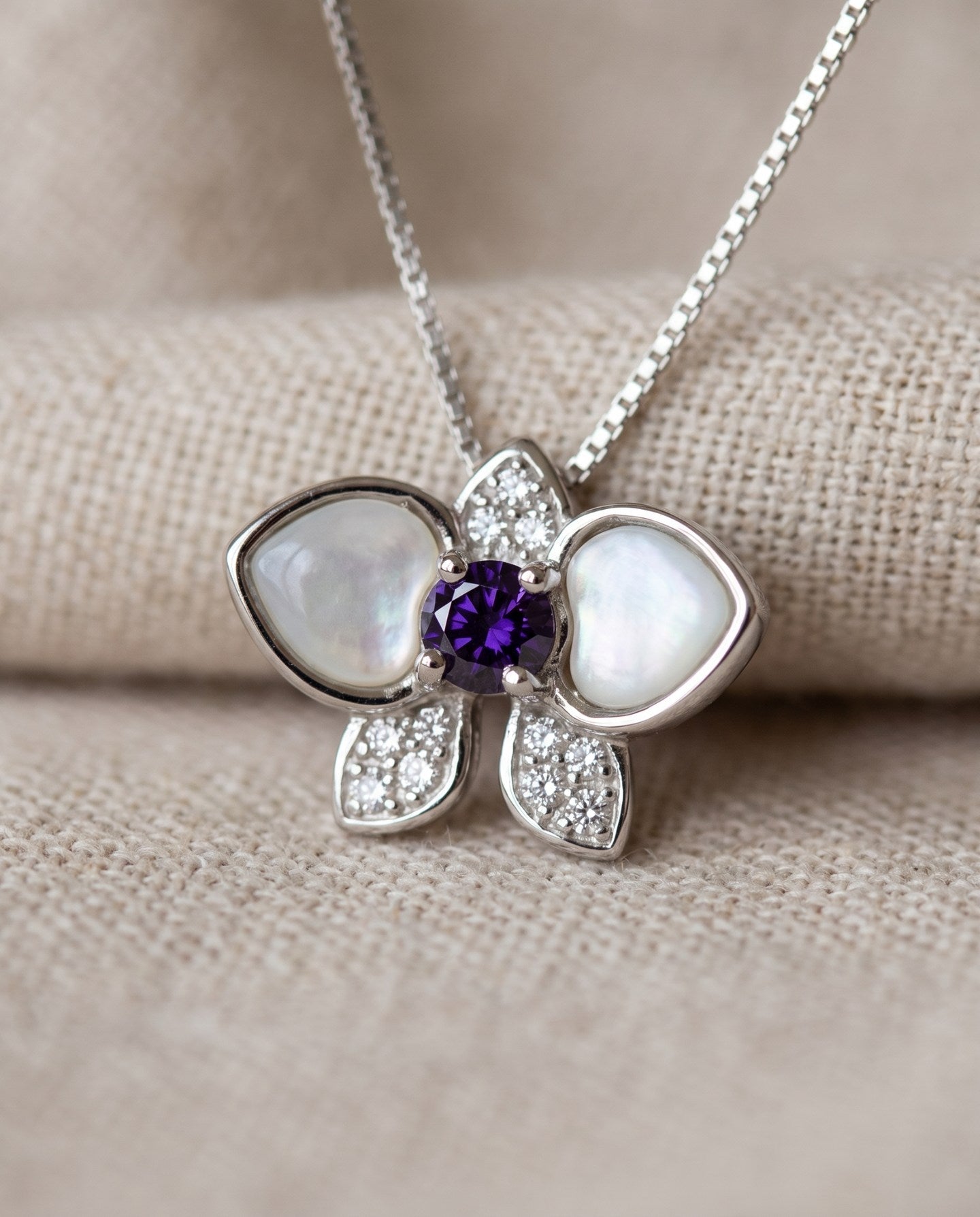 Orchid Bloom Mother of Pearl Necklace in silver with iridescent wings and purple spinel centre on a soft ivory background