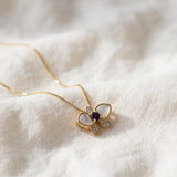 Orchid Bloom Mother of Pearl Necklace in yellow gold with iridescent wings and purple spinel centre on a soft ivory background