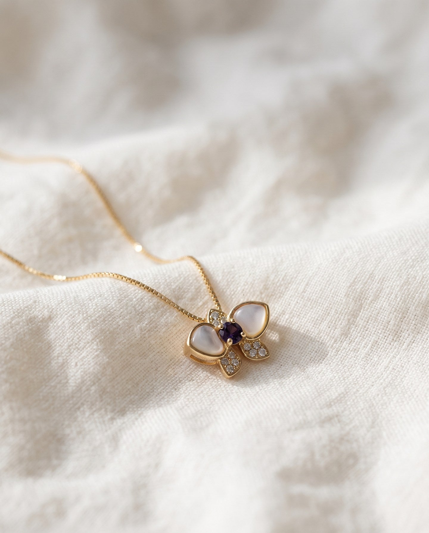 Orchid Bloom Mother of Pearl Necklace in yellow gold with iridescent wings and purple spinel centre on a soft ivory background