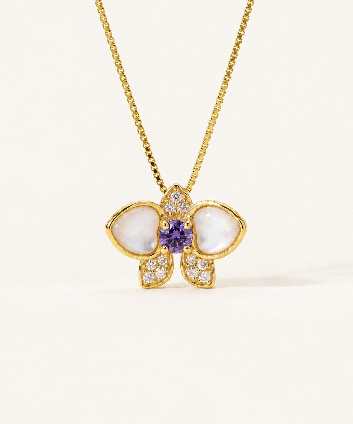 Orchid Bloom Mother of Pearl Necklace in yellow gold with iridescent wings and purple spinel centre on a soft ivory background
