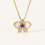 Orchid Bloom Mother of Pearl Necklace in yellow gold with iridescent wings and purple spinel centre on a soft ivory background