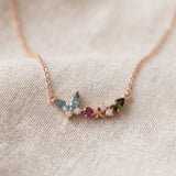 Papillon and Blossom butterfly necklace in rose gold with teal apatite, rhodolite garnet and chrome diopside on a neutral ivory background