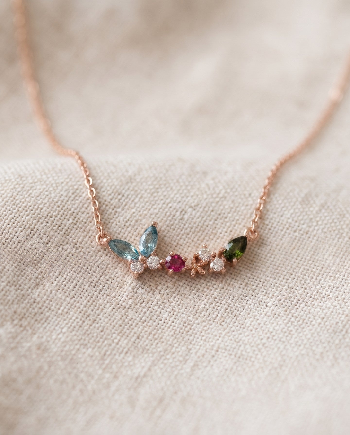 Papillon and Blossom butterfly necklace in rose gold with teal apatite, rhodolite garnet and chrome diopside on a neutral ivory background