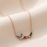 Papillon and Blossom butterfly necklace in rose gold with teal apatite, rhodolite garnet and chrome diopside on a neutral ivory background