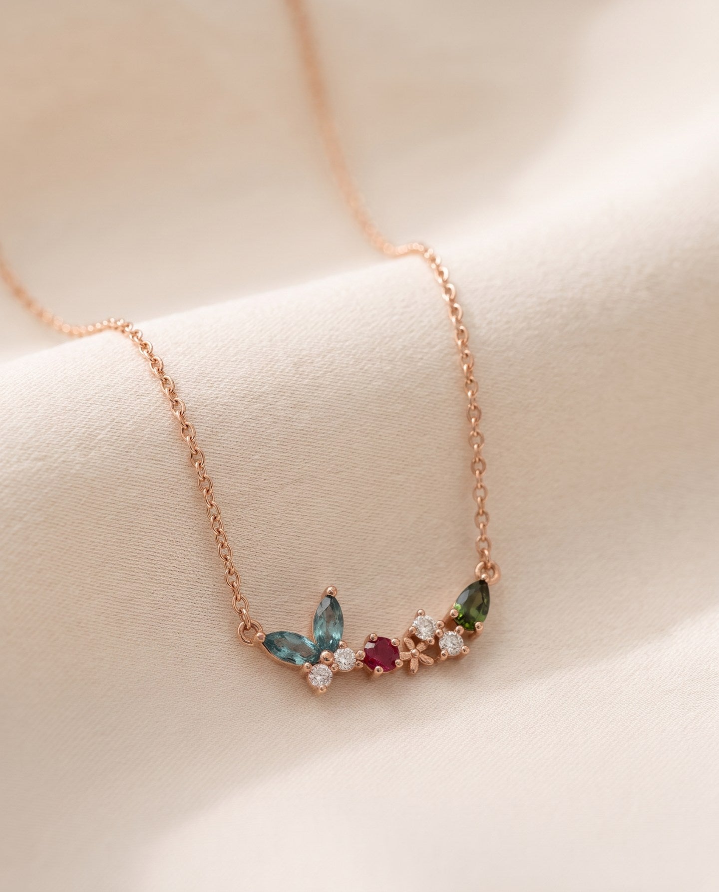 Papillon and Blossom butterfly necklace in rose gold with teal apatite, rhodolite garnet and chrome diopside on a neutral ivory background