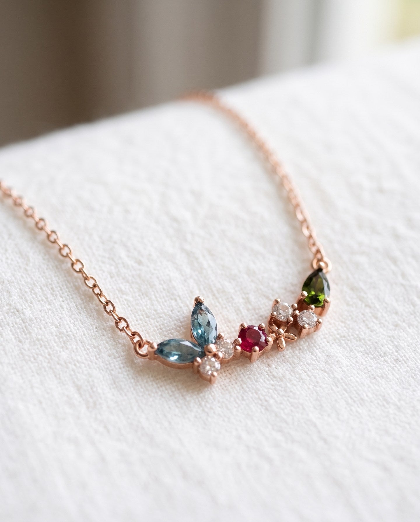 Papillon and Blossom butterfly necklace in rose gold with teal apatite, rhodolite garnet and chrome diopside on a neutral ivory background
