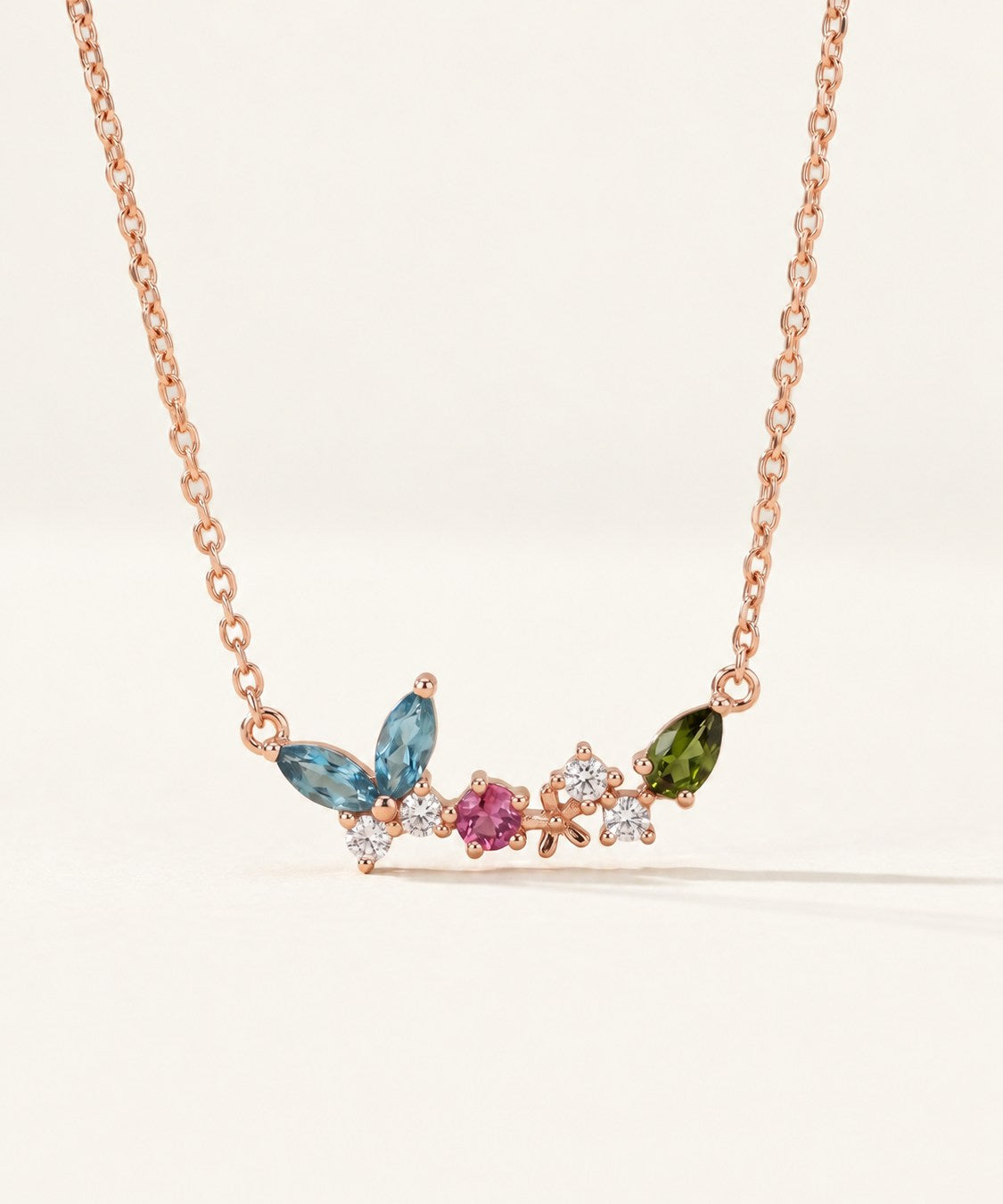 Papillon and Blossom butterfly necklace in rose gold with teal apatite, rhodolite garnet and chrome diopside on a neutral ivory background