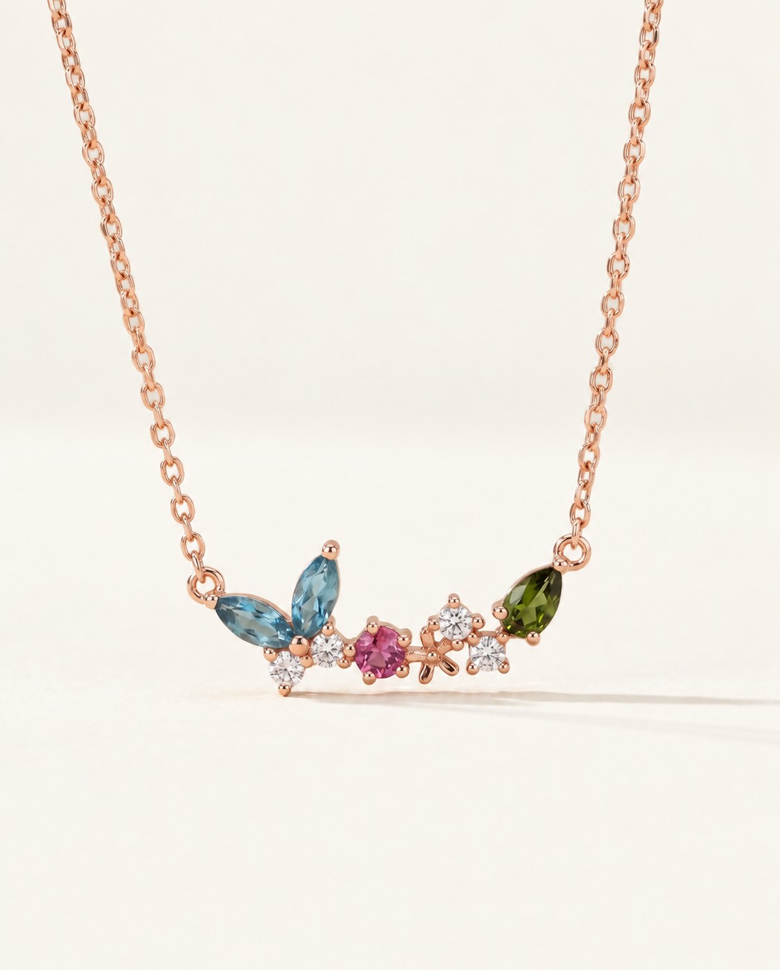 Papillon and Blossom butterfly necklace in rose gold with teal apatite, rhodolite garnet and chrome diopside on a neutral ivory background