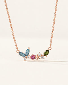 Papillon and Blossom butterfly necklace in rose gold with teal apatite, rhodolite garnet and chrome diopside on a neutral ivory background