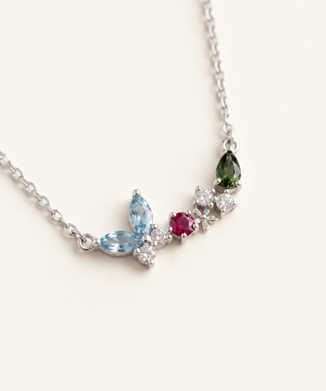 Papillon and Blossom butterfly necklace in silver with teal apatite, rhodolite garnet and chrome diopside on a neutral ivory background