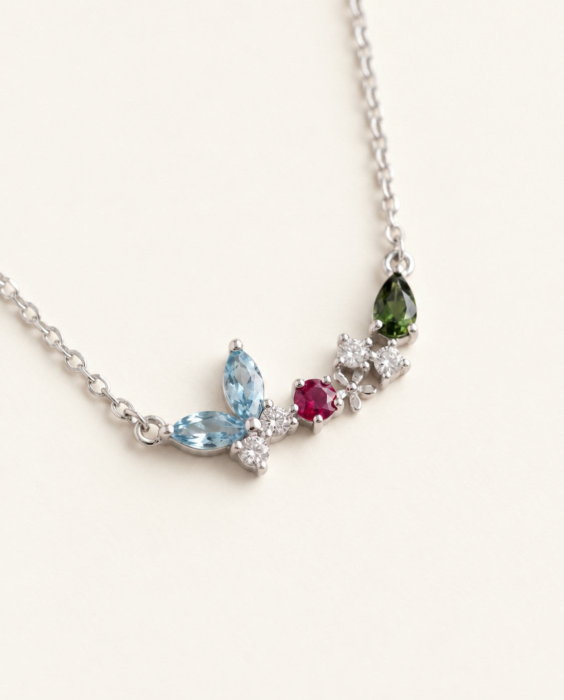Papillon and Blossom butterfly necklace in silver with teal apatite, rhodolite garnet and chrome diopside on a neutral ivory background