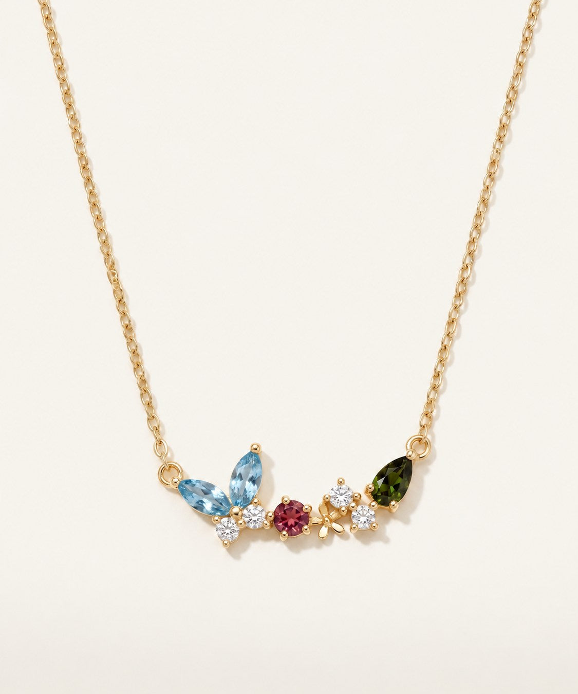 Papillon and Blossom butterfly necklace in yellow gold with teal apatite, rhodolite garnet and chrome diopside on a neutral ivory background