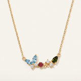 Papillon and Blossom butterfly necklace in yellow gold with teal apatite, rhodolite garnet and chrome diopside on a neutral ivory background