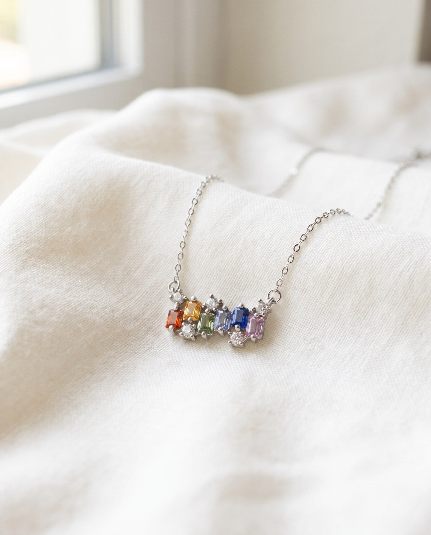 Prism Baguette Rainbow Sapphire Necklace in silver with six multicolour natural sapphires on a neutral ivory background