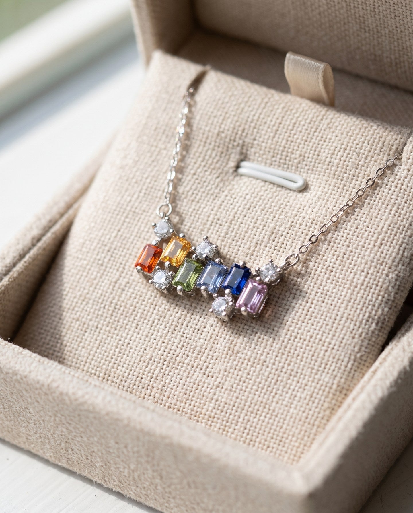 Prism Baguette Rainbow Sapphire Necklace in silver with six multicolour natural sapphires on a neutral ivory background