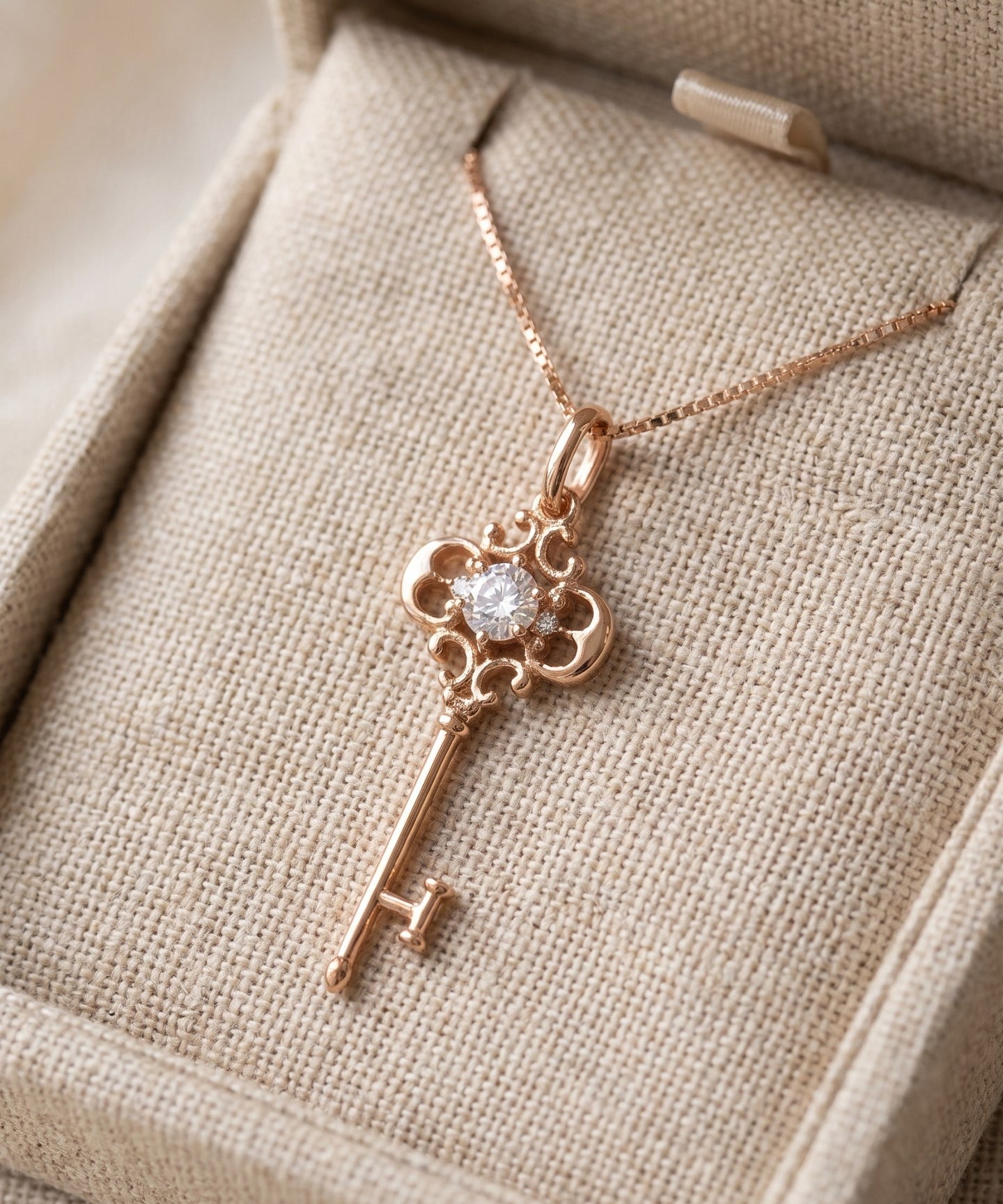 Memoir Grey Moissanite Key Necklace in rose gold, styled on neutral fabric